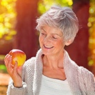 Woman with dental implants in Huntington Beach holding an apple.