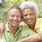 Older couple with dental implants in Huntington Beach smiling outside.