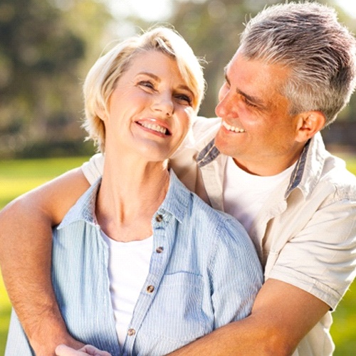 A middle-aged couple hugging and smiling after receiving their dental implants