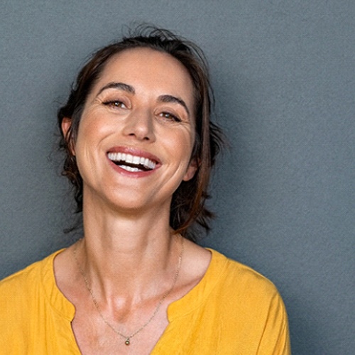 Happy woman in yellow shirt smiling after osseous surgery