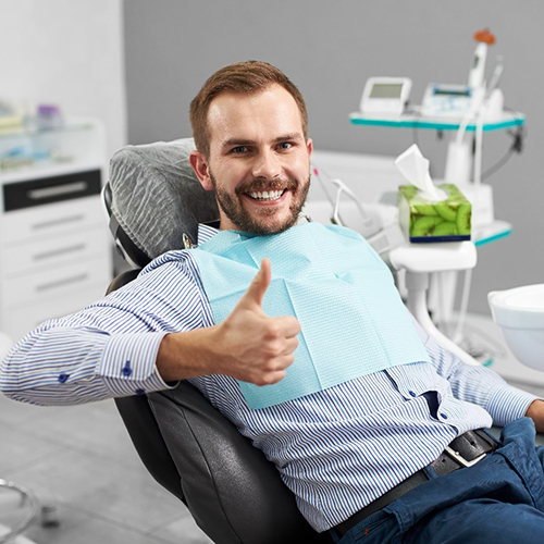 Smiling man sitting on dental chair and giving thumb’s up