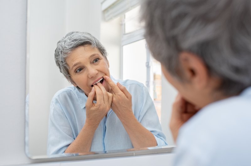 Older woman flossing dental implants in Orange County