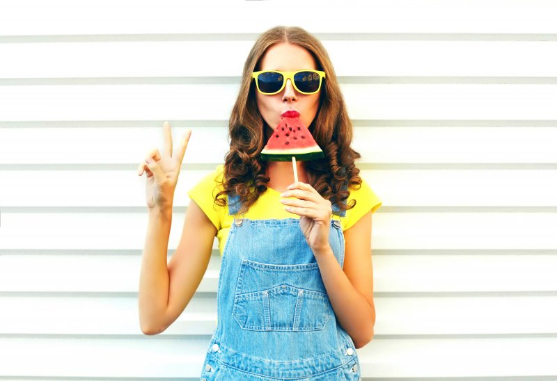 Woman eating watermelon on a stick.