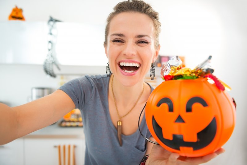 A woman smiling with a small bucket of Halloween candy thinking about oral health